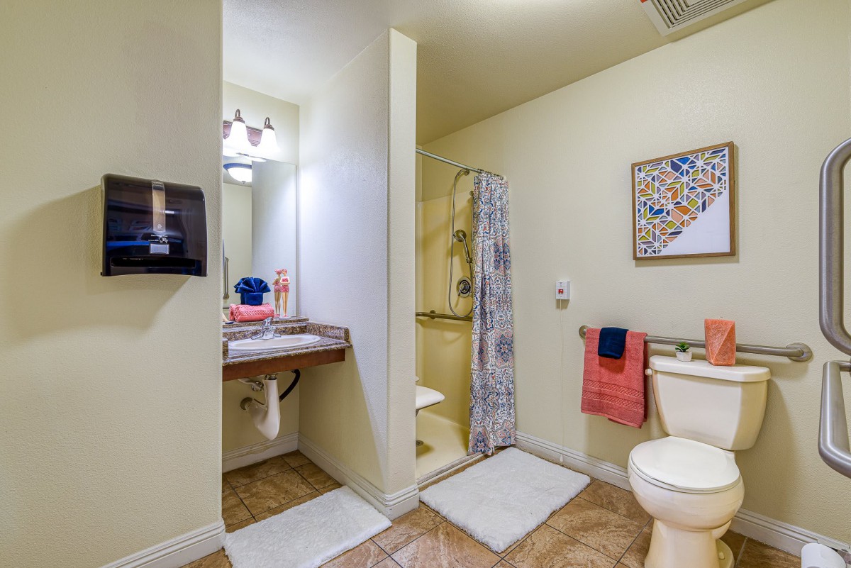 A well-lit bathroom featuring a sink, shower, and toilet with colorful towels and decor.