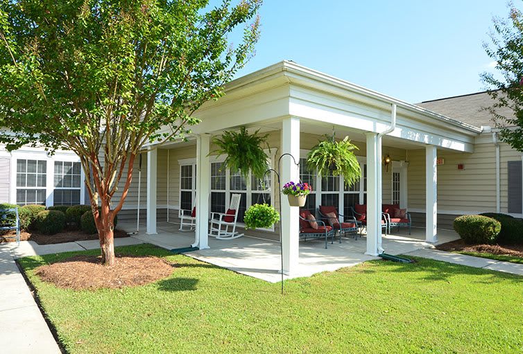 A cozy porch with outdoor seating surrounded by a well-maintained garden and trees.