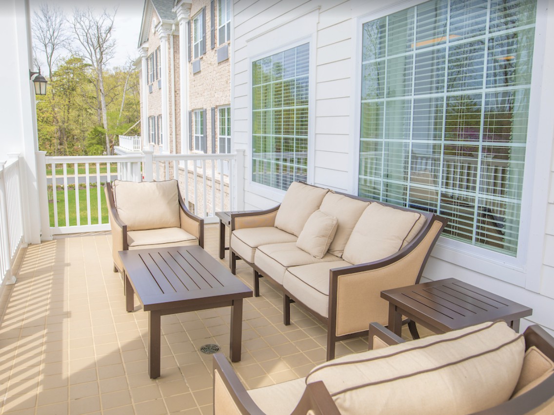 A cozy outdoor patio with cushioned seating and a coffee table, adjacent to a house with large windows.