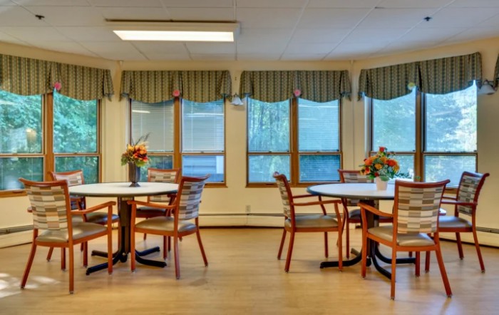 A cozy dining area with round tables, chairs, and large windows adorned with curtains.