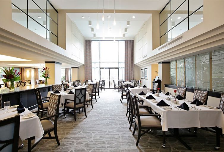 A spacious and elegant restaurant interior with tables set under white tablecloths and abundant natural light.