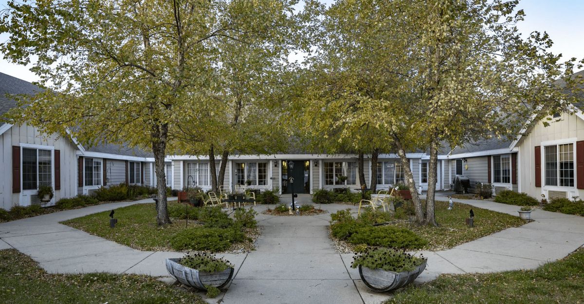 A landscaped pathway leading to a building entrance, surrounded by trees and plants.