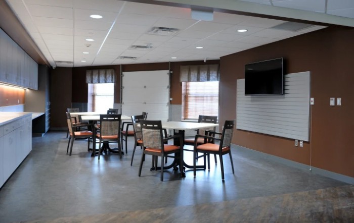 A modern dining area with tables and chairs, featuring a wall-mounted television and large windows.