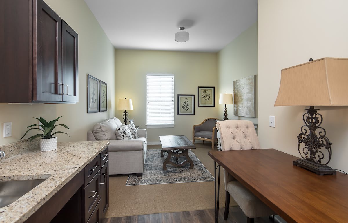 A cozy living room with a sofa, armchair, coffee table, and desk, softly lit by lamps.