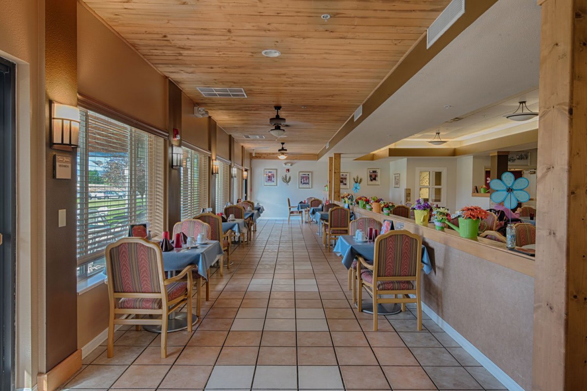 A cozy restaurant dining area with neatly arranged tables and chairs, ambient lighting, and a wooden ceiling.