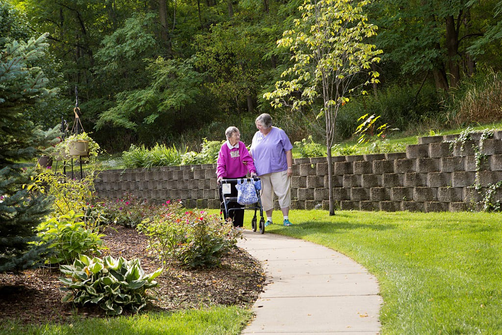 Two elderly individuals walking on a pathway surrounded by greenery.