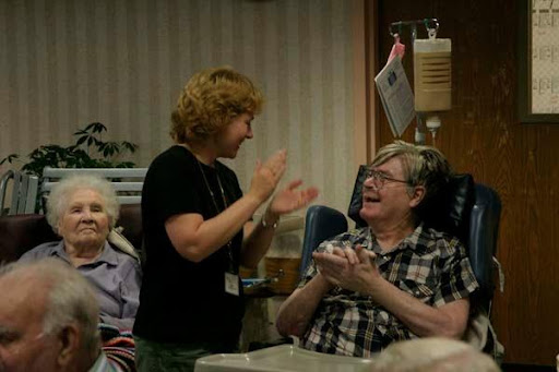 A joyful interaction between a caregiver and a resident in a nursing home, filled with applause and smiles.