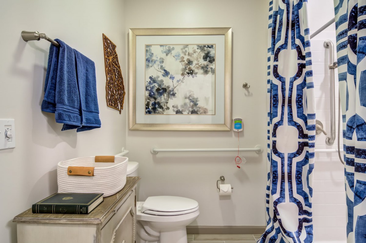 A well-decorated bathroom with a blue patterned shower curtain, artwork on the wall, and neatly folded towels.