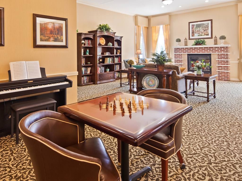 A cozy living room with a chess table, piano, fireplace, and bookshelves.