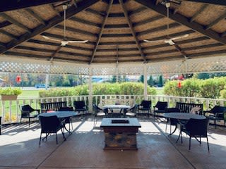 A cozy outdoor gazebo with seating and a central fire pit, surrounded by lush greenery.