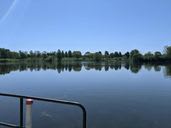 A serene view of a lake with trees reflecting on the calm water under a clear blue sky.