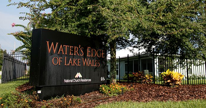 Entrance sign for Water's Edge of Lake Wales surrounded by trees and landscaping.