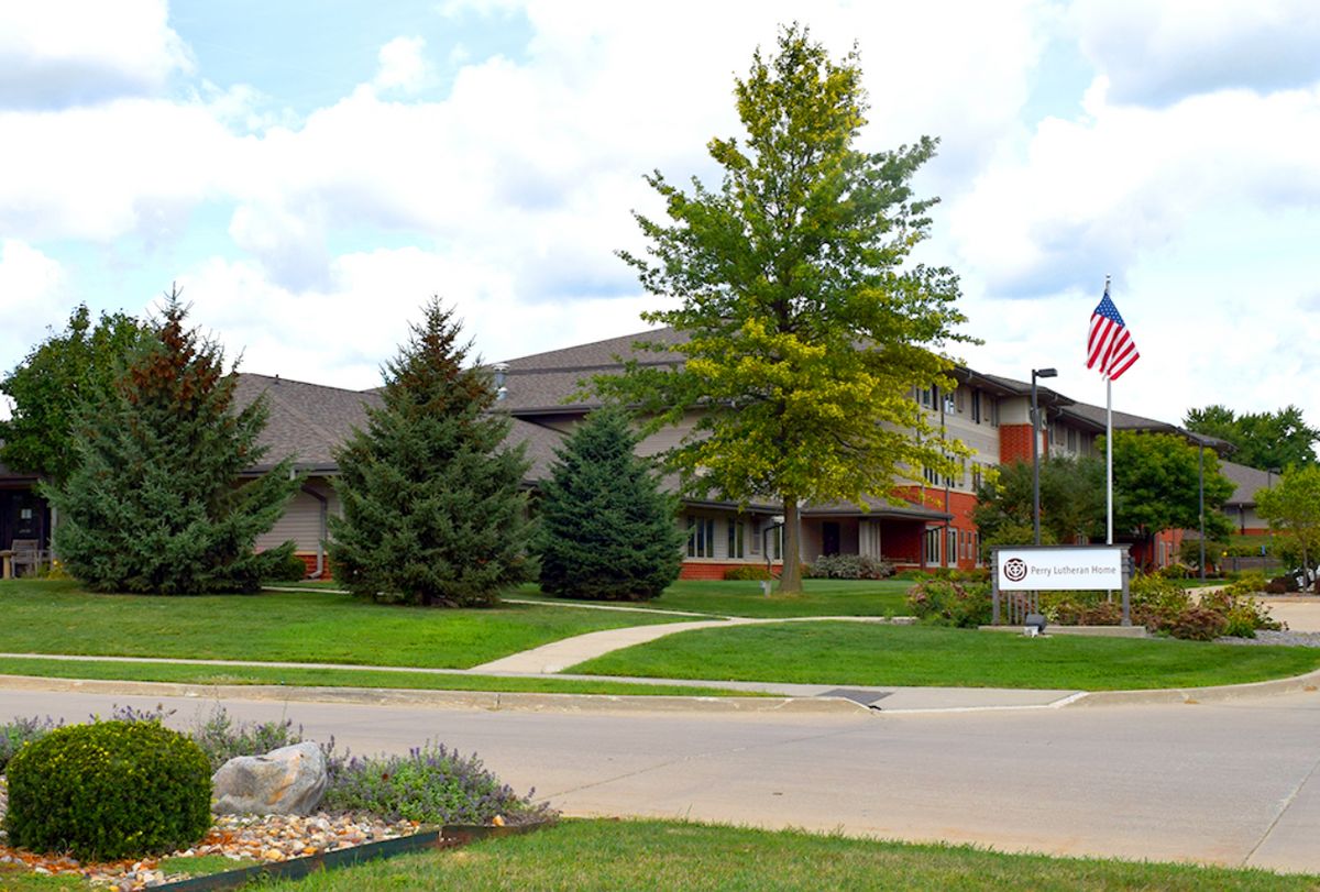 A building surrounded by greenery with a flag and a driveway.