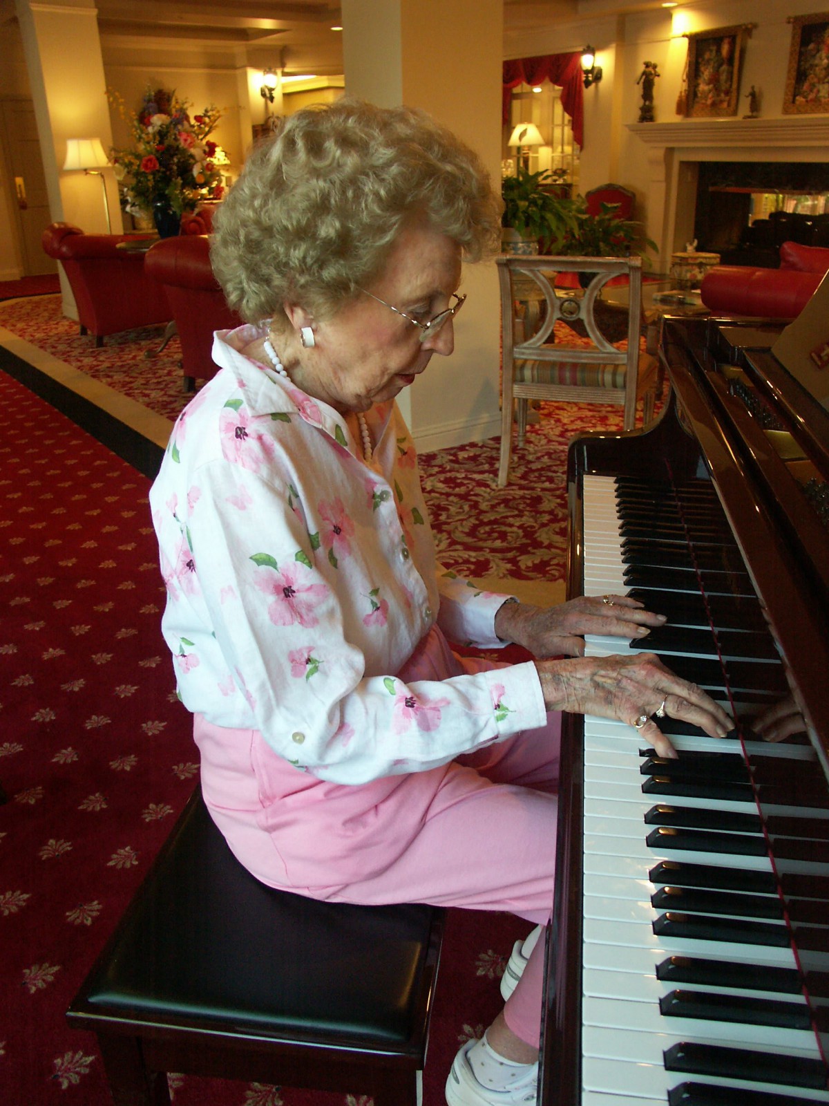 An elderly woman playing the piano indoors.