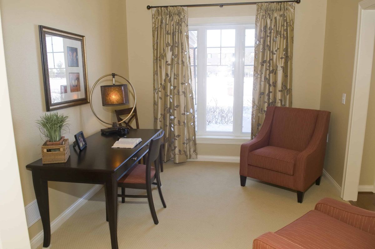 A cozy home office featuring a desk, chair, and window with curtains.