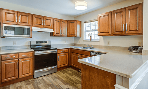 A modern kitchen with wooden cabinets, featuring an oven and stove, sink, and ample countertop space.