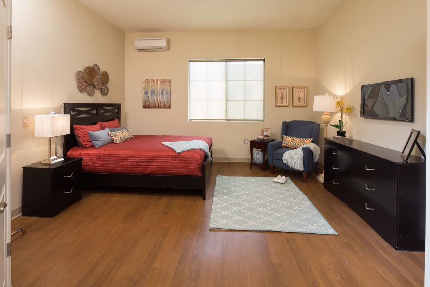 A cozy bedroom with red bedding, wooden flooring, and a comfortable armchair by the window.