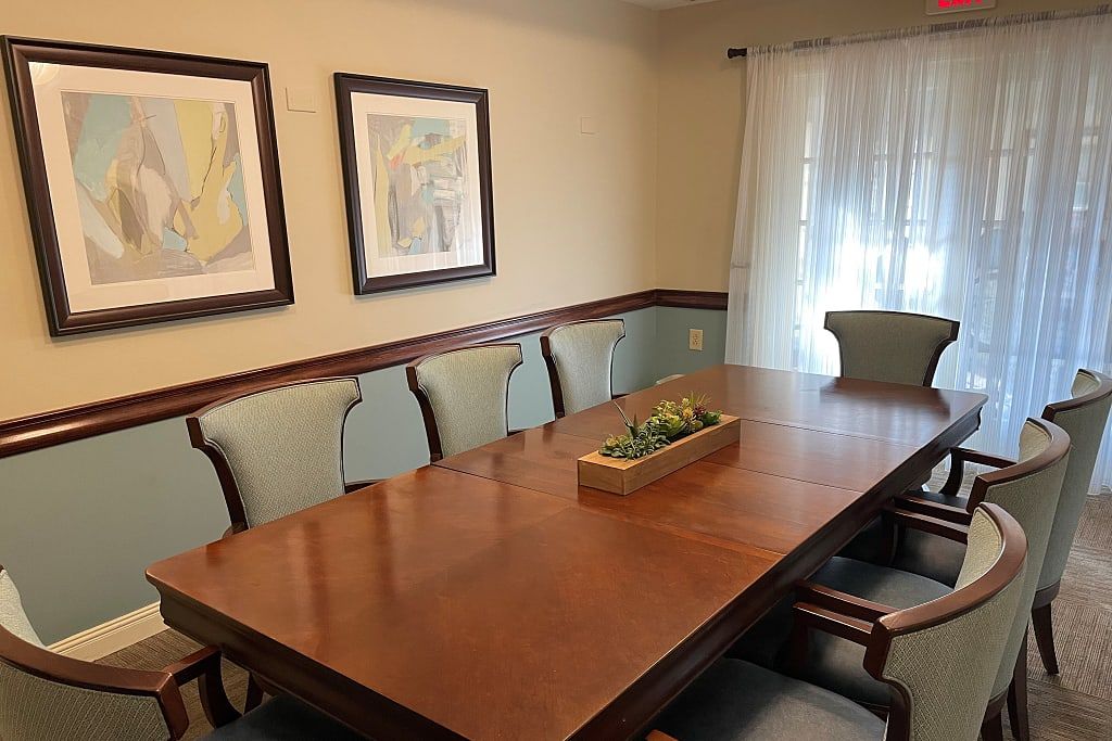 A dining room featuring a large wooden table surrounded by chairs, with framed artwork on the walls and a decorative centerpiece.