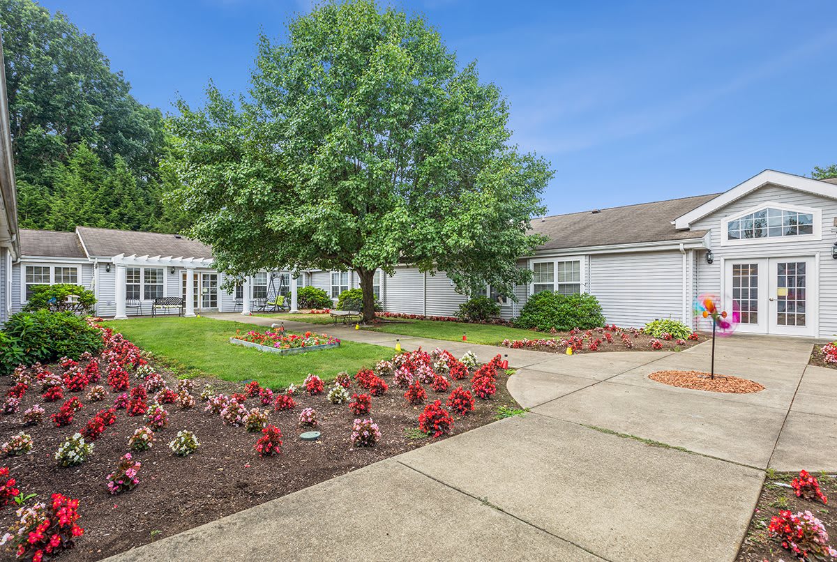 A charming house with a beautifully landscaped garden featuring colorful flowers and a large tree, set alongside a winding pathway.