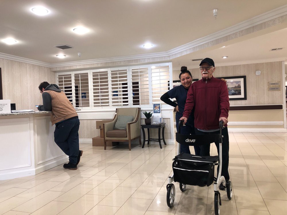 A person uses a walker accompanied by another individual in an assisted living facility.