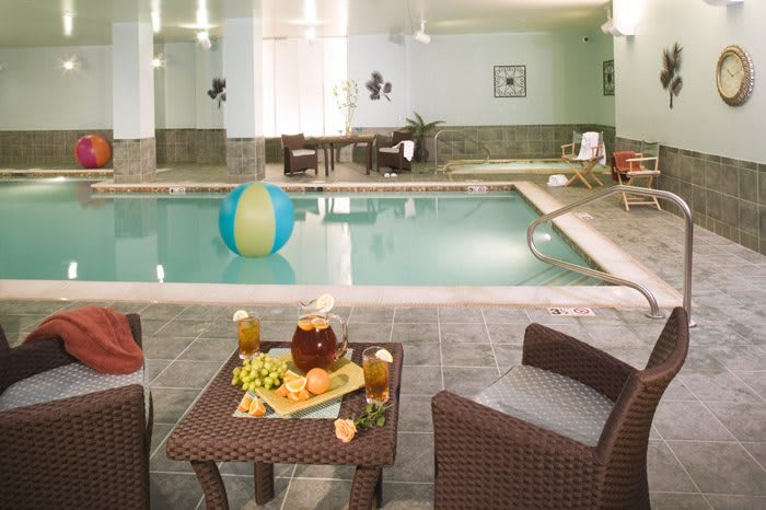 A cozy indoor swimming pool area with rattan chairs, a table set with snacks and beverages, offering a relaxing atmosphere.