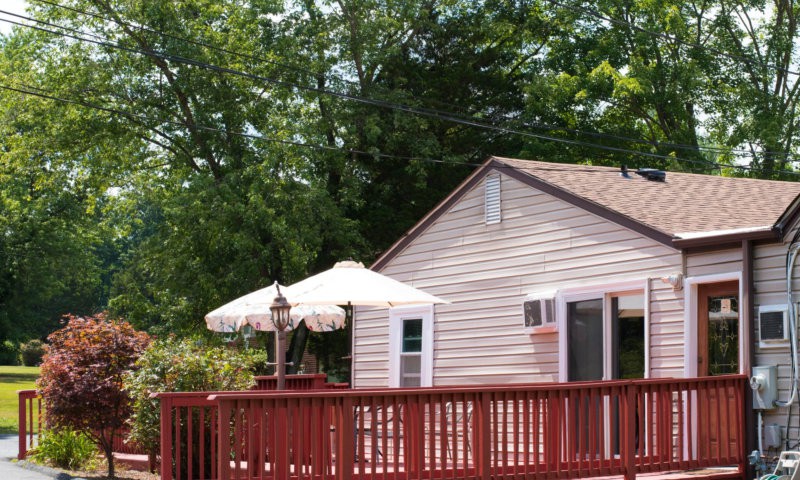 A cozy house with a wooden deck and an outdoor umbrella surrounded by lush trees.