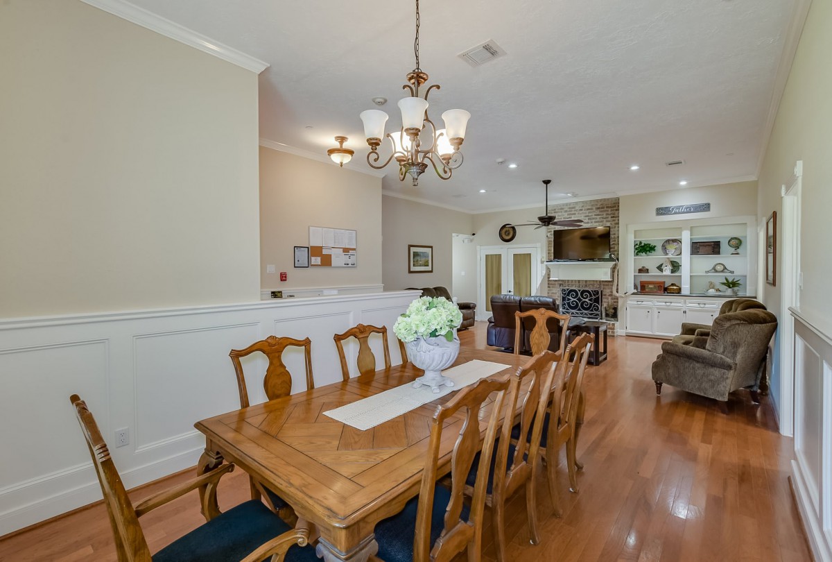A spacious dining area with wooden furniture and a chandelier, featuring an open layout connected to the kitchen.