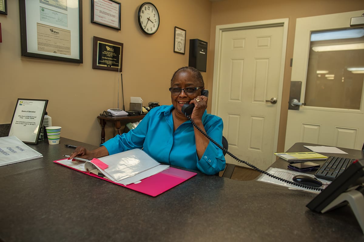A woman in an office speaking on the phone with files on her desk.