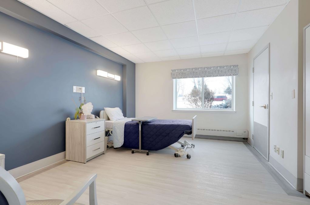 A clean and minimalist hospital room with a single bed and a large window.