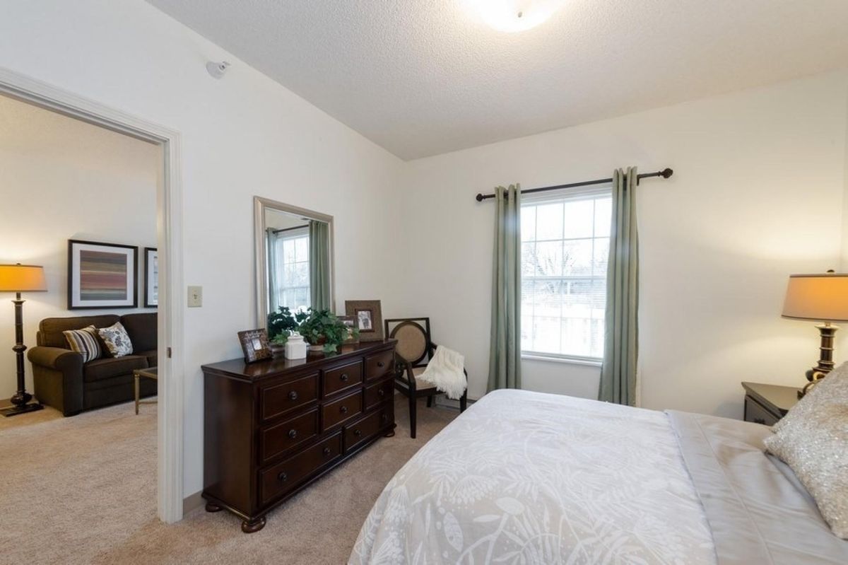 A cozy bedroom featuring a wooden dresser, a large mirror, and a bed with white linens.