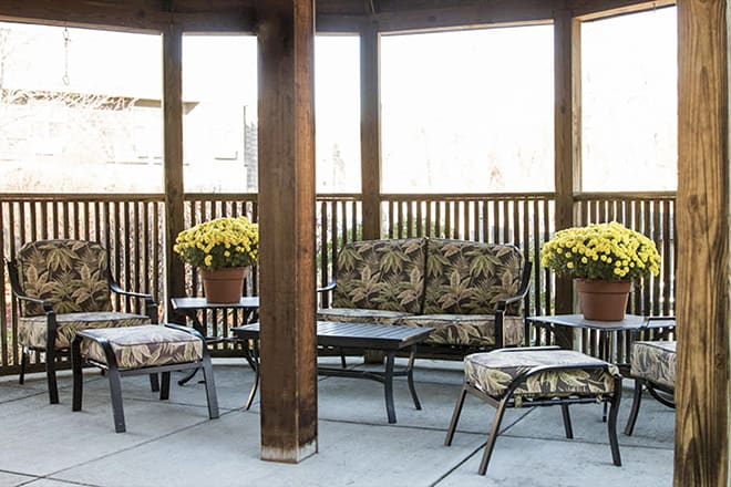 A cozy patio setup with cushioned outdoor furniture and potted yellow flowers under a wooden gazebo.