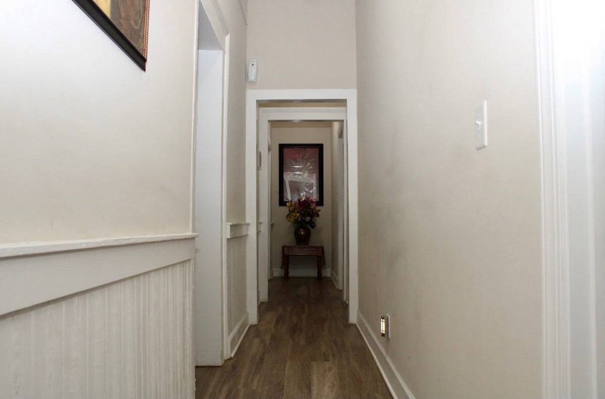 A narrow hallway with wood flooring and white walls, featuring doorways leading to other rooms.