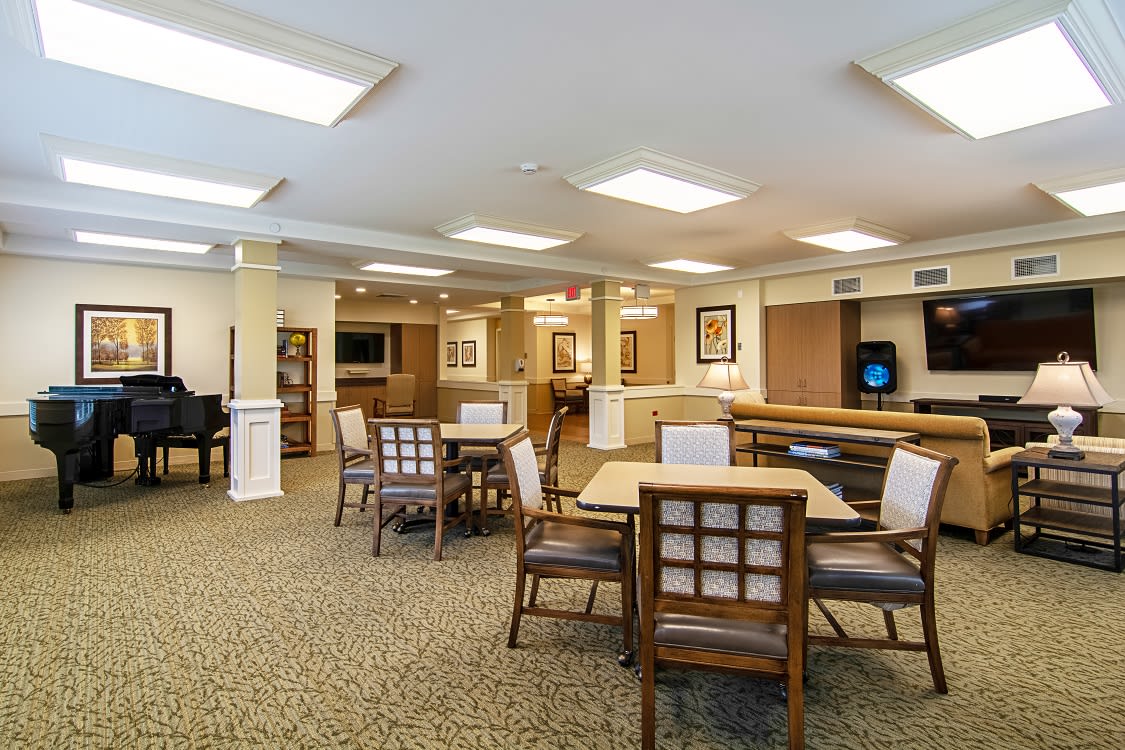 A spacious lounge area with tables and chairs, illuminated by ceiling lights.