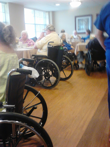 A social gathering in an assisted living facility where several elderly individuals are seated in wheelchairs.