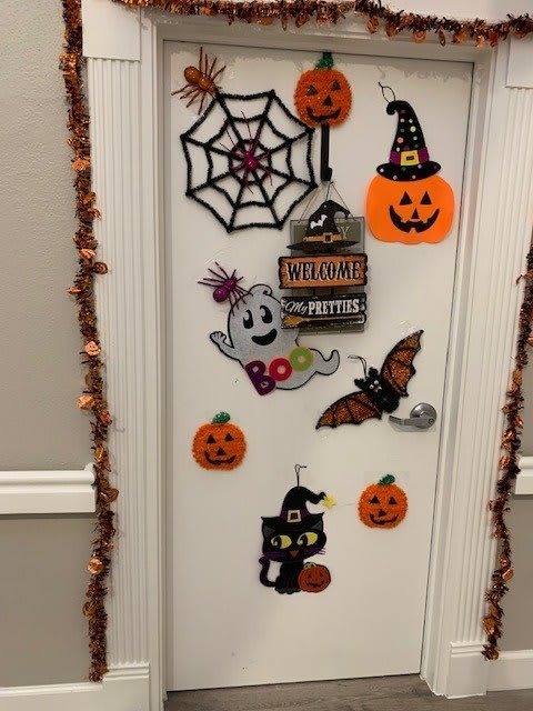 A door decorated with festive Halloween-themed decorations including a spider web, pumpkins, a ghost, a bat, and a cat with a witch hat.