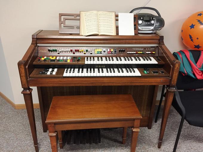 A vintage organ with a wooden bench, sheet music, and a cassette player on top.