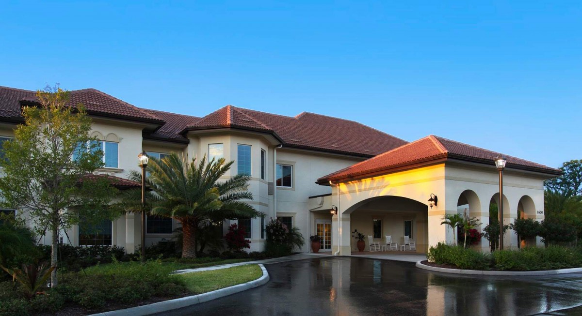 A modern building with a red-tiled roof and palm tree landscaping, featuring an inviting entrance and driveway.