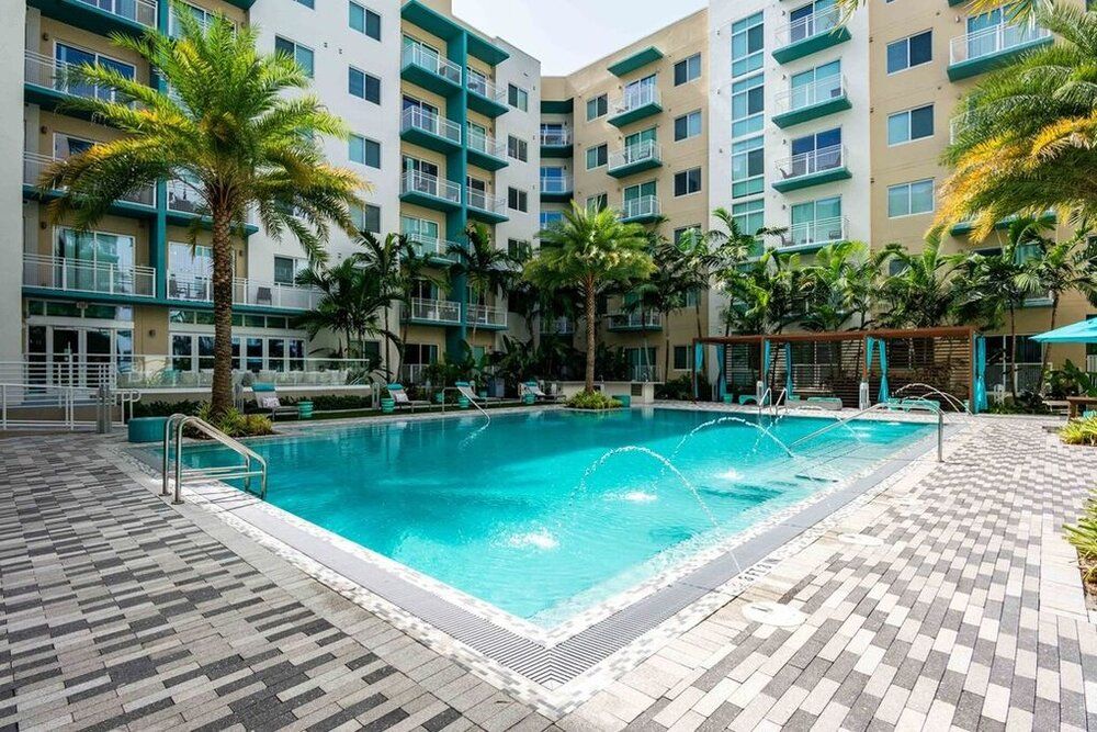 Modern apartment complex with a swimming pool and palm trees.