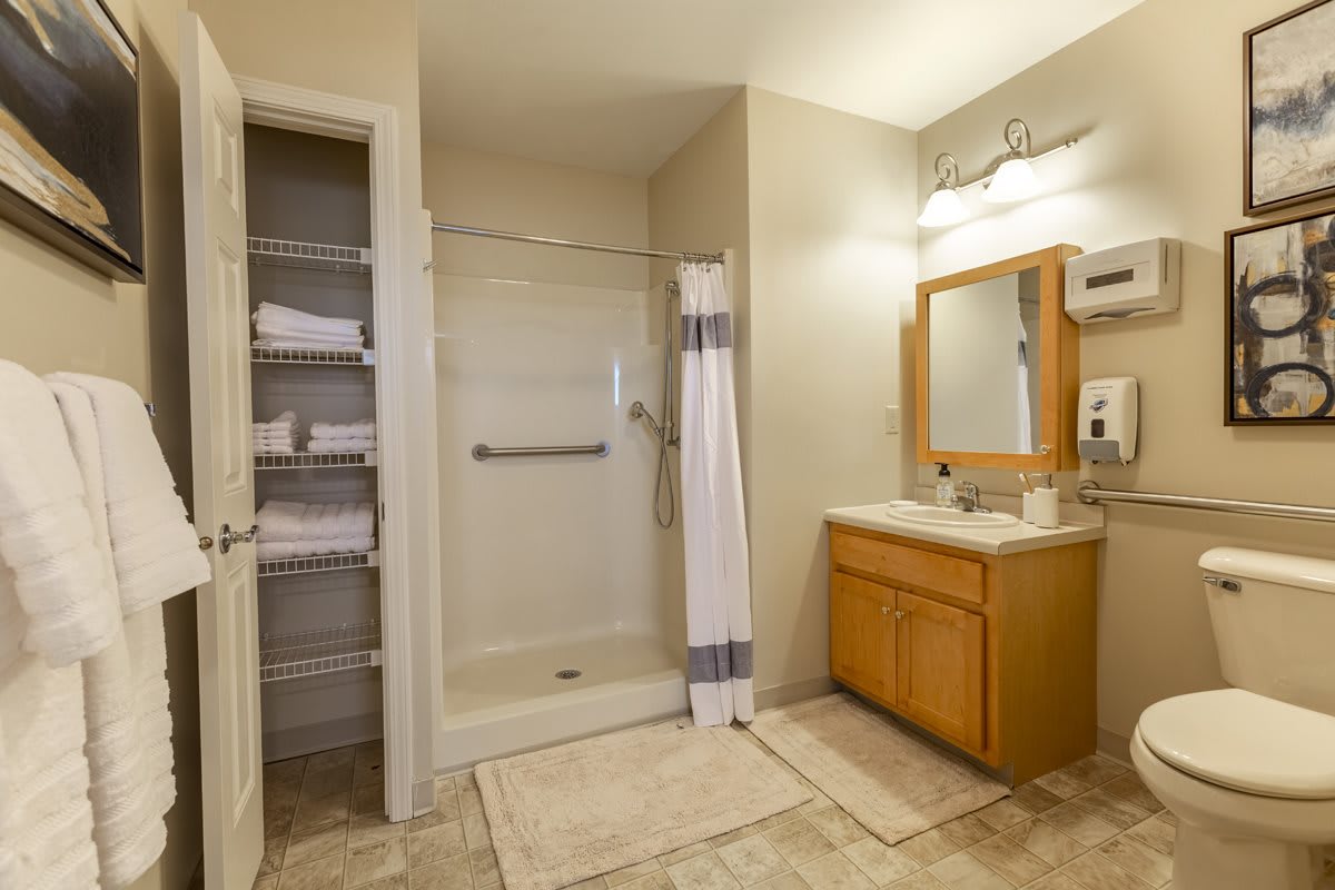 A well-organized bathroom featuring a shower, vanity with mirror, and neatly stacked towels.