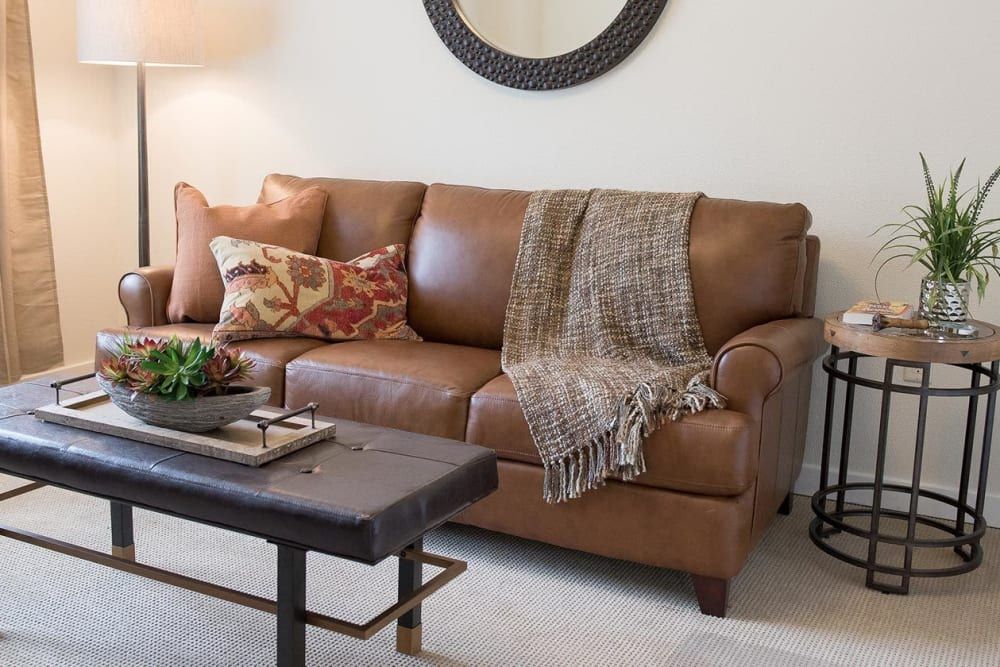 A cozy living room with a brown leather sofa adorned with cushions and a throw, next to a stylish coffee table.