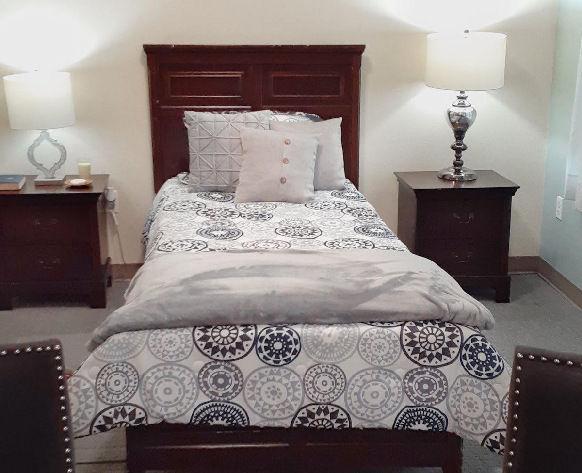A cozy bedroom with a single bed, flanked by nightstands and lamps, featuring decorative bedding.