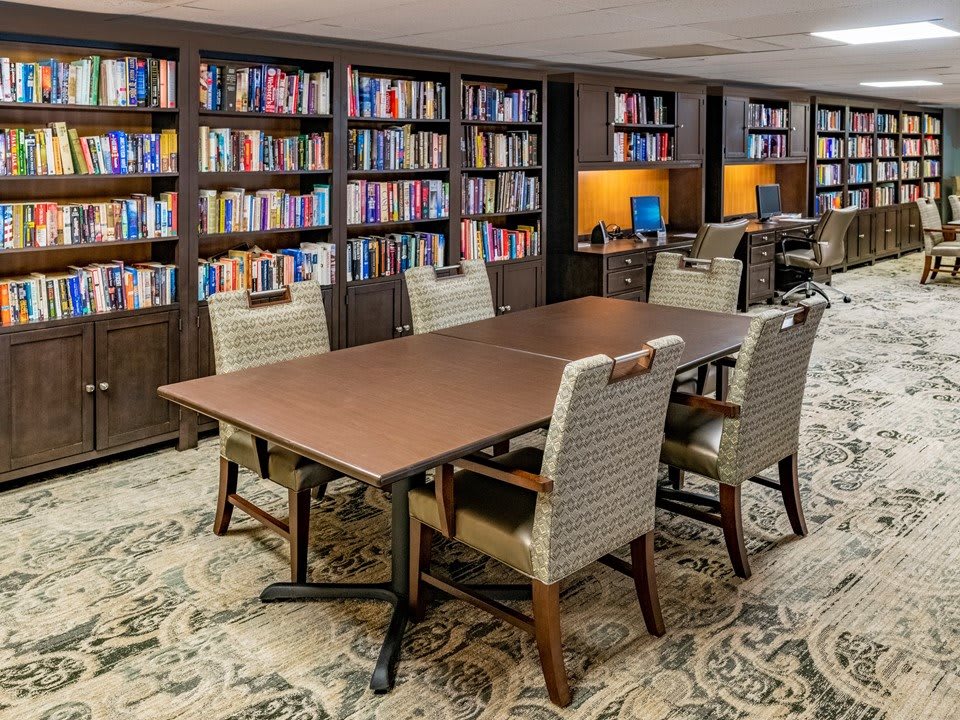 A cozy library reading area with a large table, surrounded by bookshelves filled with books.