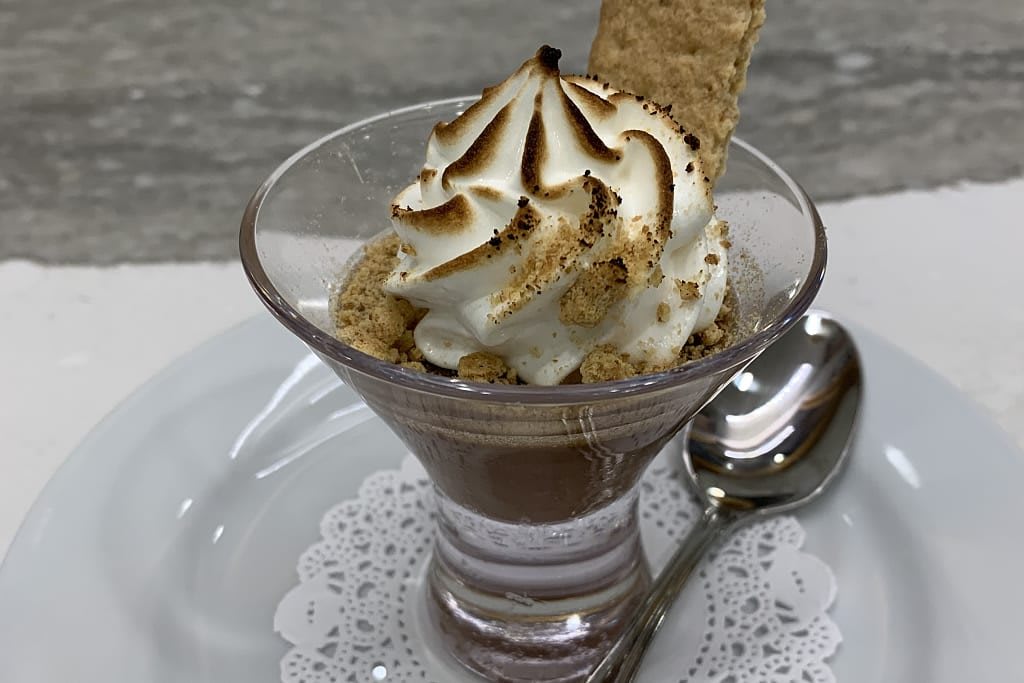 A delectable chocolate mousse topped with whipped cream and a graham cracker, elegantly served in a glass cup.