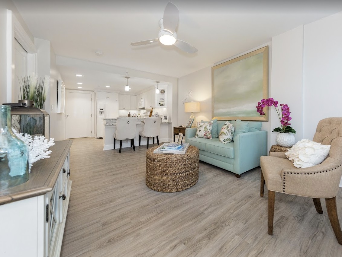 A modern living room with an open floor plan, featuring pastel-colored furnishings and wood flooring.