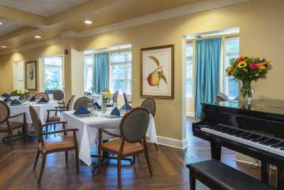 An elegant dining room with neatly arranged tables, a piano, and tasteful decor.