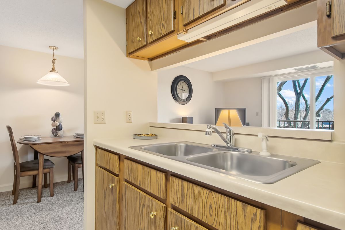 A cozy kitchen with a dual sink and wooden cabinets, opening into a living space.