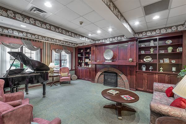 A traditional-style living room with a piano, fireplace, and bookshelves.