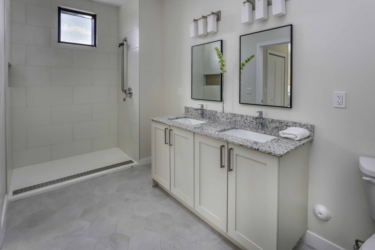 A modern bathroom featuring a double sink vanity with granite countertops and a spacious walk-in shower.