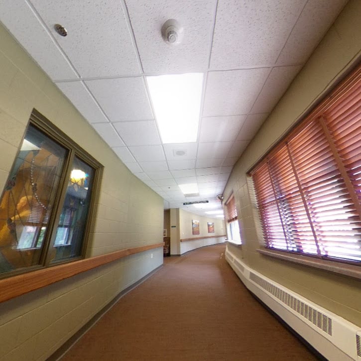 A view of a hallway with windows on one side and ceiling lights illuminating the space.