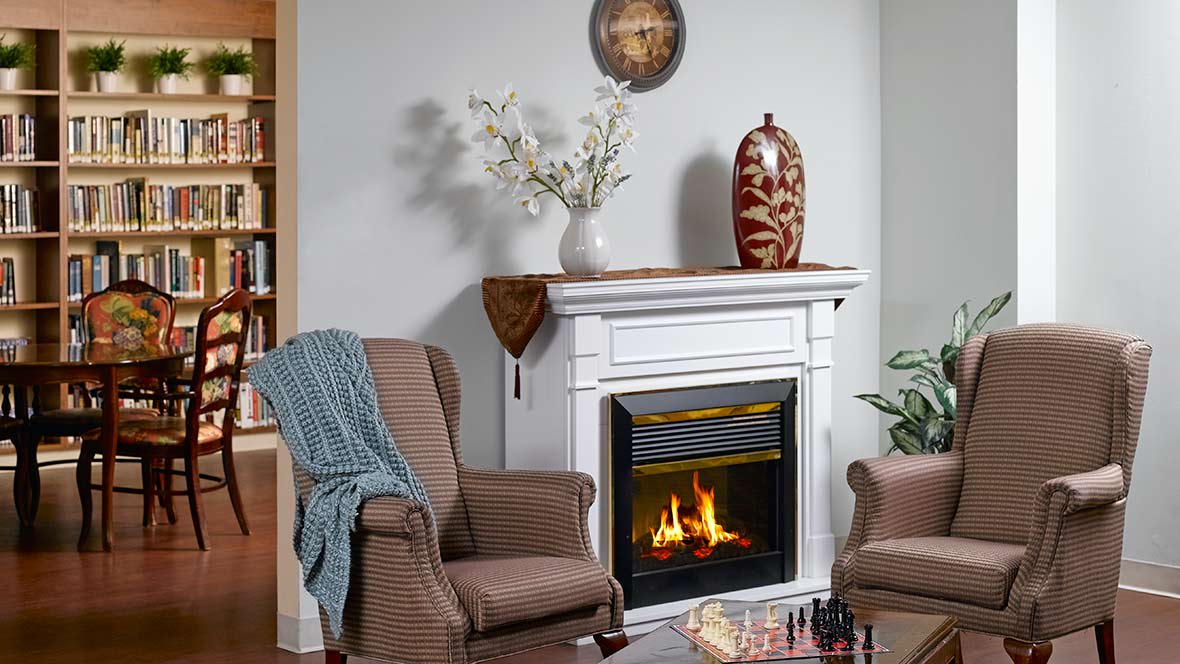 A cozy living room with a fireplace and armchairs, featuring decorative elements like a vase and wall art.